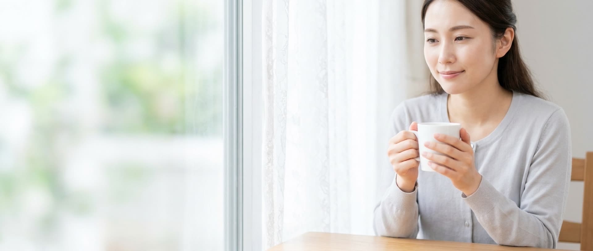 明るいダイニングでマグカップを手に、落ち着いた表情で考える女性
